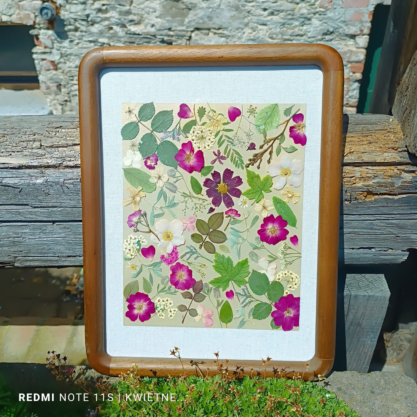 An arrangement on lace fabric featuring pressed clover leaves, rose petals, a floral sketch on paper, a small decorative pouch, a cross pendant box, a colorful beaded cross, crystals, and a small cork bottle with decorative faux flowers.